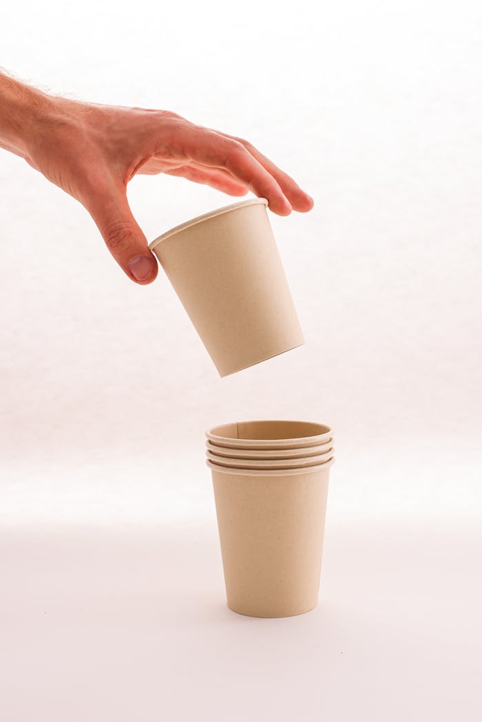 Close-up of a hand stacking biodegradable paper cups on a neutral background.