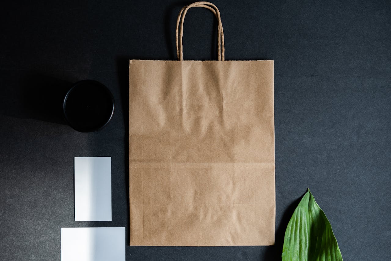 Stylish flat lay composition featuring a brown paper bag, green leaf, and black cup on a dark background.